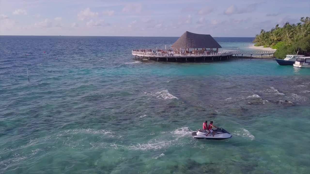 航拍拍摄的游客在海上骑水上摩托艇对天空，无人机飞过海滩在阳光明媚的一天-南马累环礁，马尔代夫视频素材