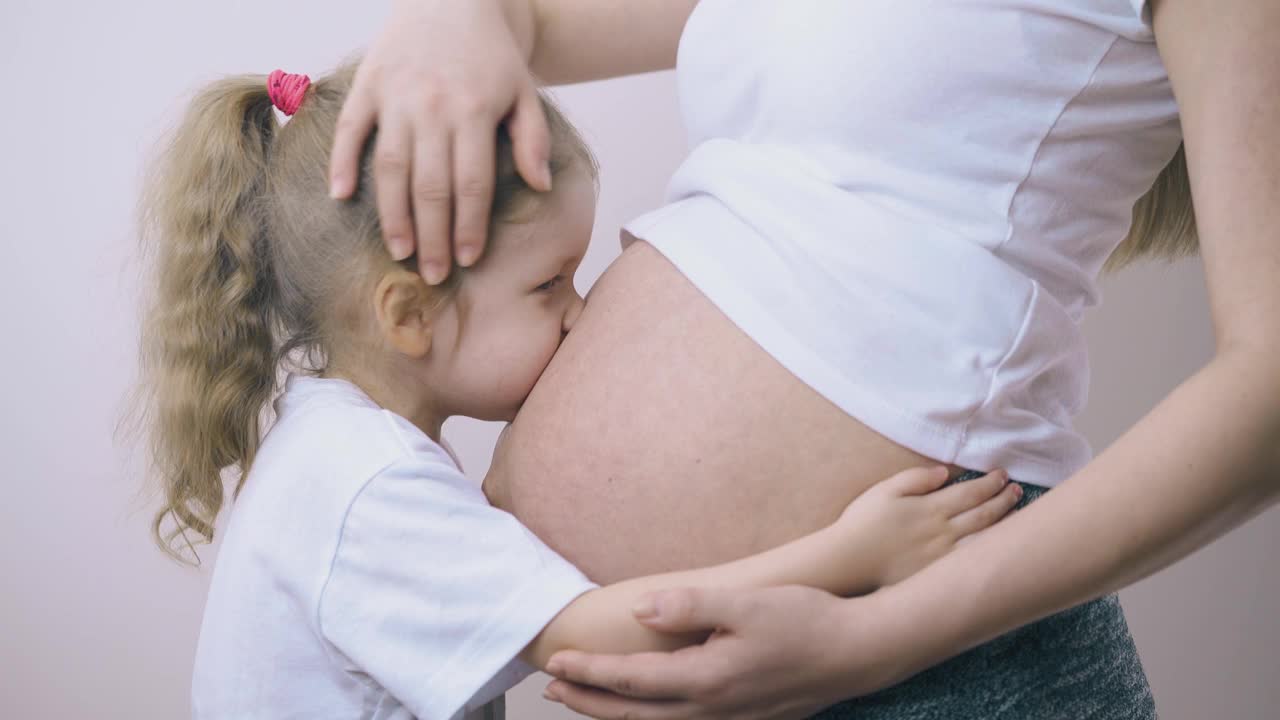 快乐的女孩在房间里亲吻孕妇的大肚子视频素材