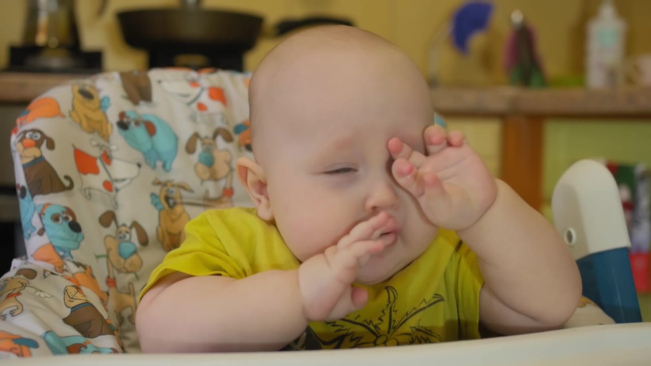 饥饿的7个月大的孩子坐在儿童椅上等待喂食。一脸不满的孩子视频素材画面1