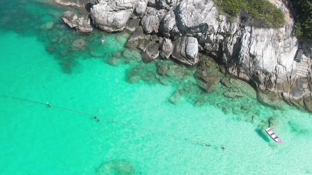 一名男子在阳光明媚的日子里在清澈的水面上浮潜悬崖附近的鸟瞰图视频素材