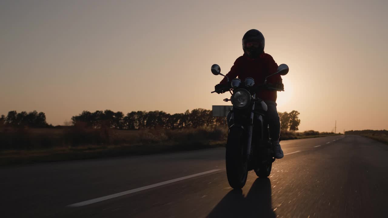 一个骑摩托车的人的剪影，在夕阳下骑在高速公路上视频素材