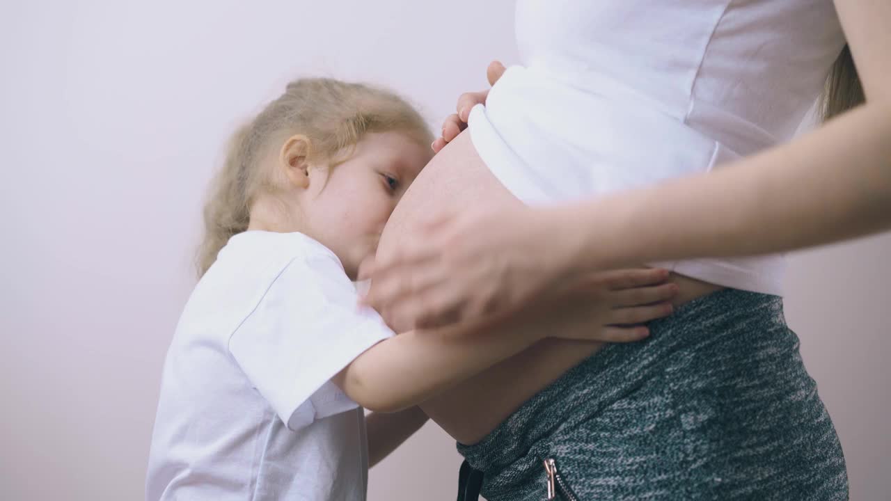 女孩亲吻孕妇听宝宝说话的大肚子视频素材