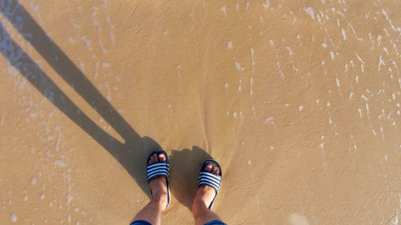 海浪冲刷着男人的脚，年轻的印度男子站在海边，享受海边的潮汐旅行，盖伊在海边享受暑假。印度古吉拉特邦Shivrajpur海滩视频素材