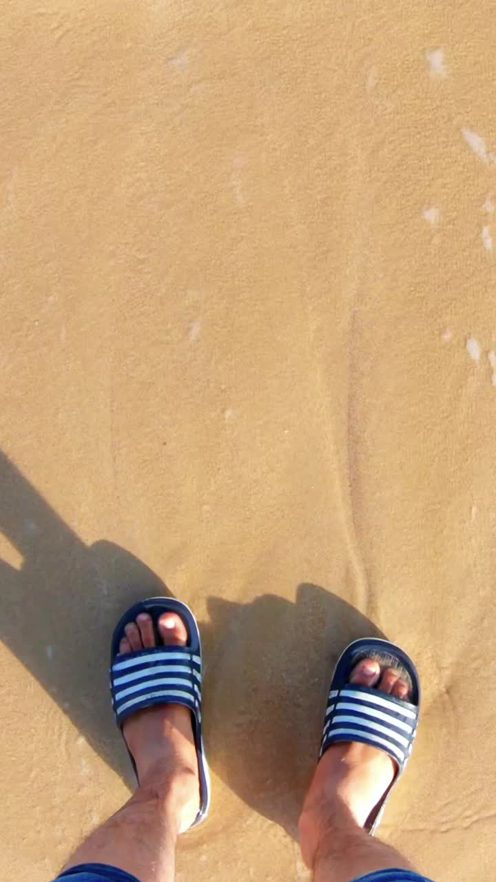 海浪冲刷着男人的脚，年轻的印度男子站在海边，享受海边的潮汐旅行，盖伊在海边享受暑假。印度古吉拉特邦Shivrajpur海滩视频素材