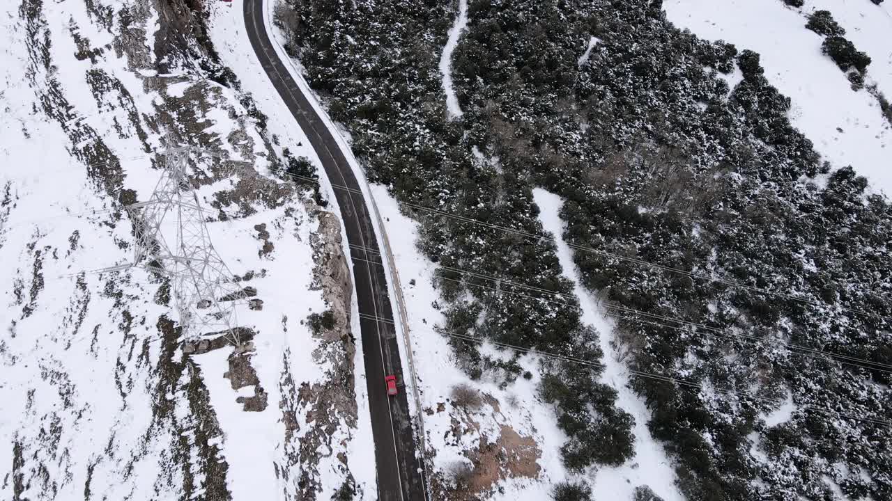 从无人机鸟瞰一辆红色汽车在冰雪路面上行驶在冬天探索当地景观，鸟瞰汽车在美丽的针叶林周围移动的区域。视频素材