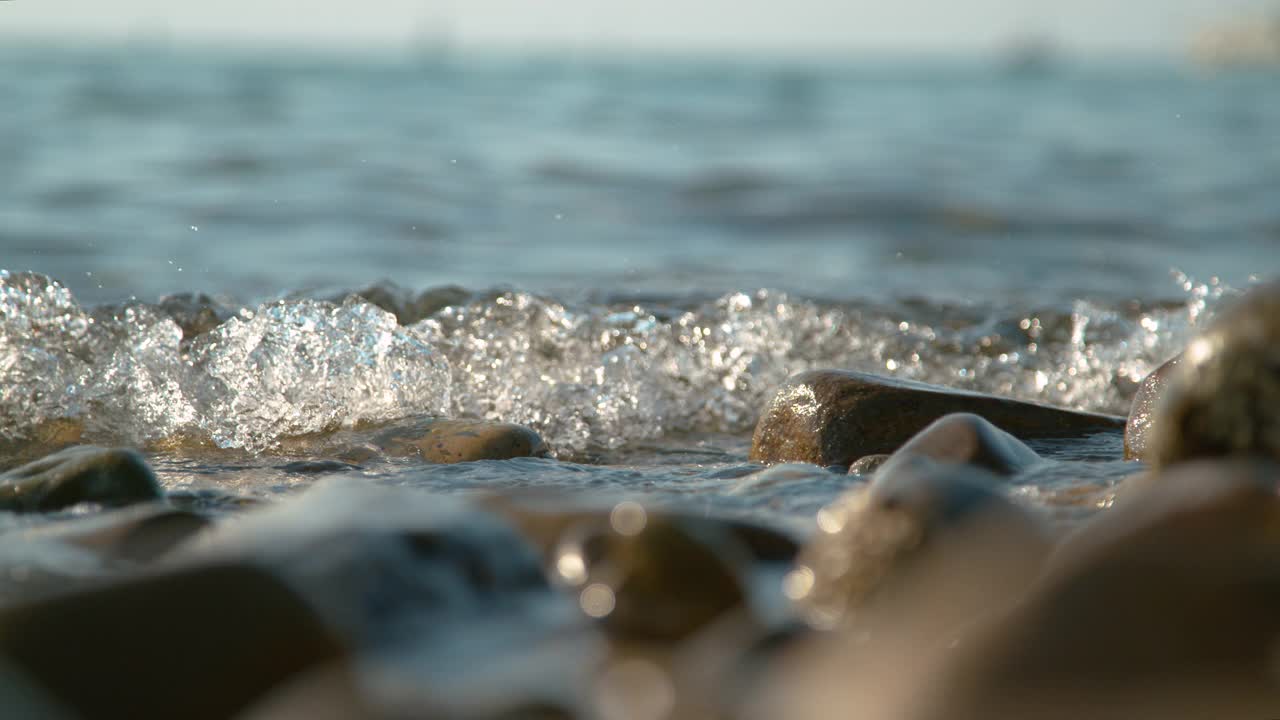 近景:空旷的海岸上，透明的海水溅在棕色的鹅卵石上。视频素材