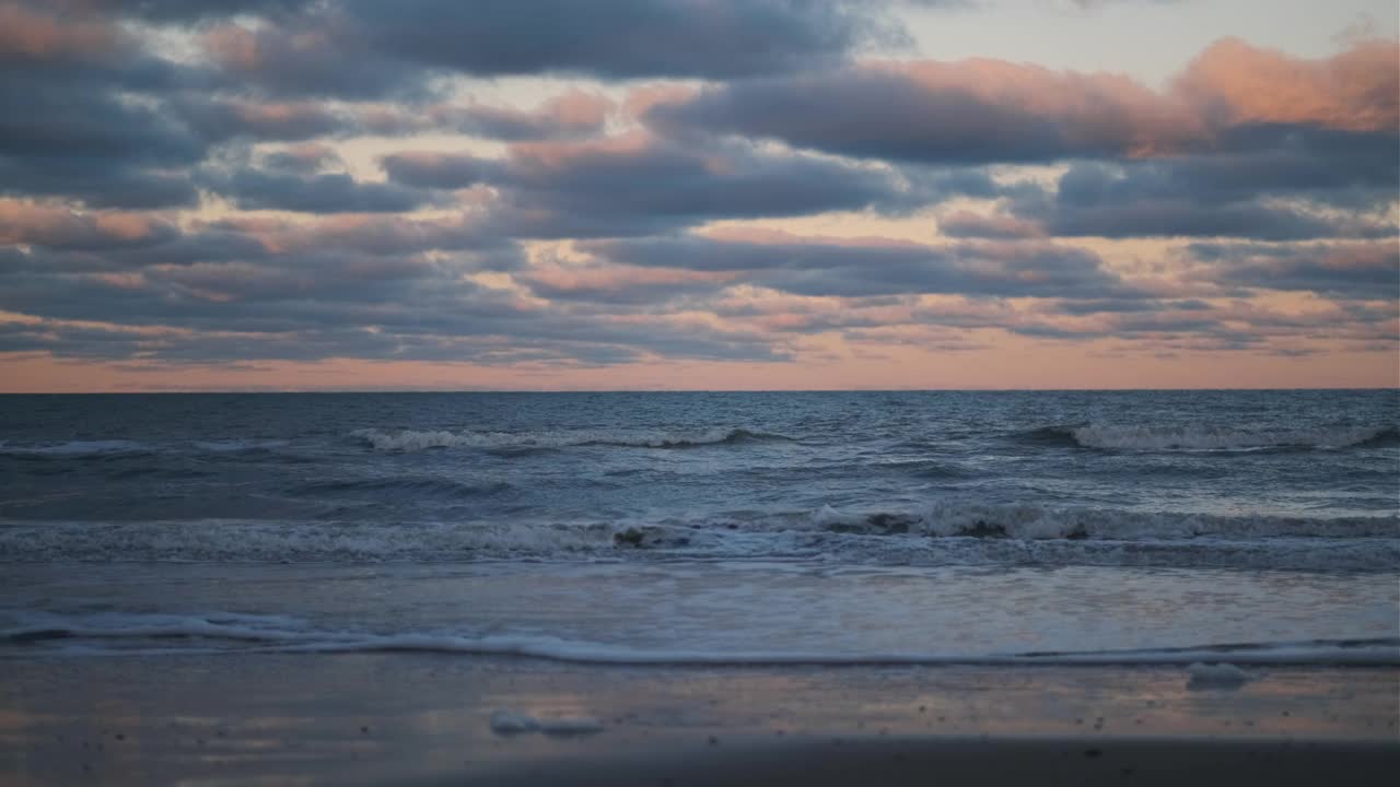 在地平线上日落时，海浪翻滚到海滩上视频素材