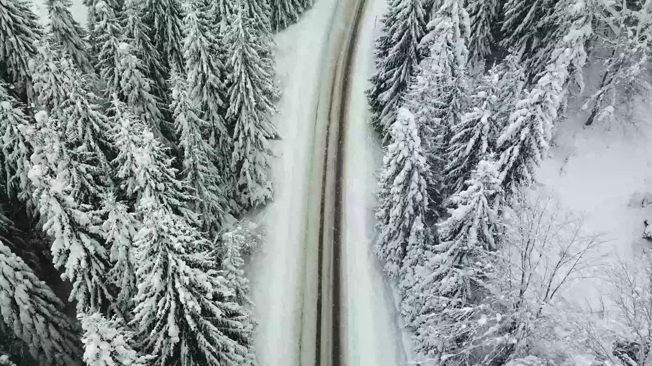 汽车行驶在冰雪覆盖的森林里的冬季乡村道路上视频素材