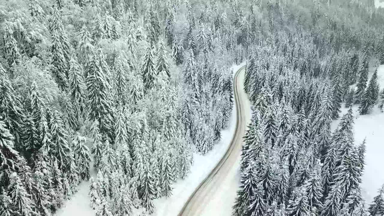 汽车行驶在冰雪覆盖的森林里的冬季乡村道路上视频素材