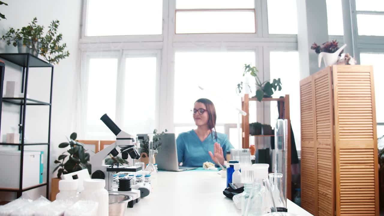 镜头拉近，有趣的年轻快乐的白种女性实验室科学家博士在桌子上跳舞，庆祝战胜冠状病毒。视频素材