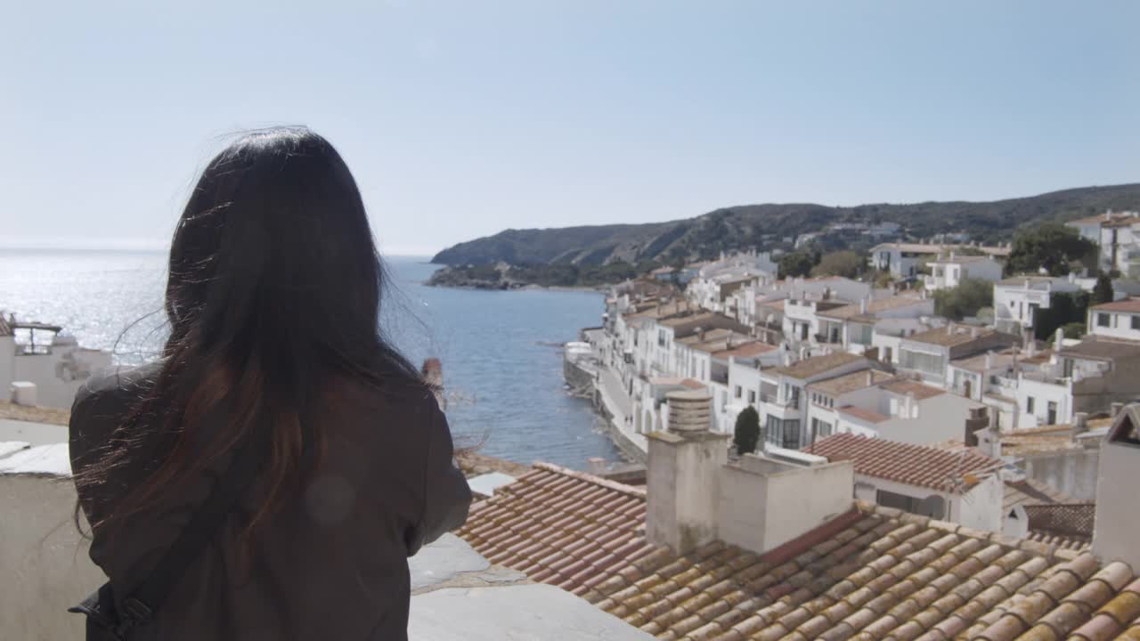 一名女游客在为Cadaqués拍照，这是一个典型的地中海村庄，有房屋和瓦片屋顶视频素材