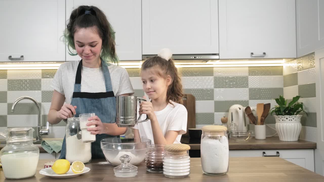 两个女孩在厨房里一起做饼干。孩子们用筛子筛面粉视频素材