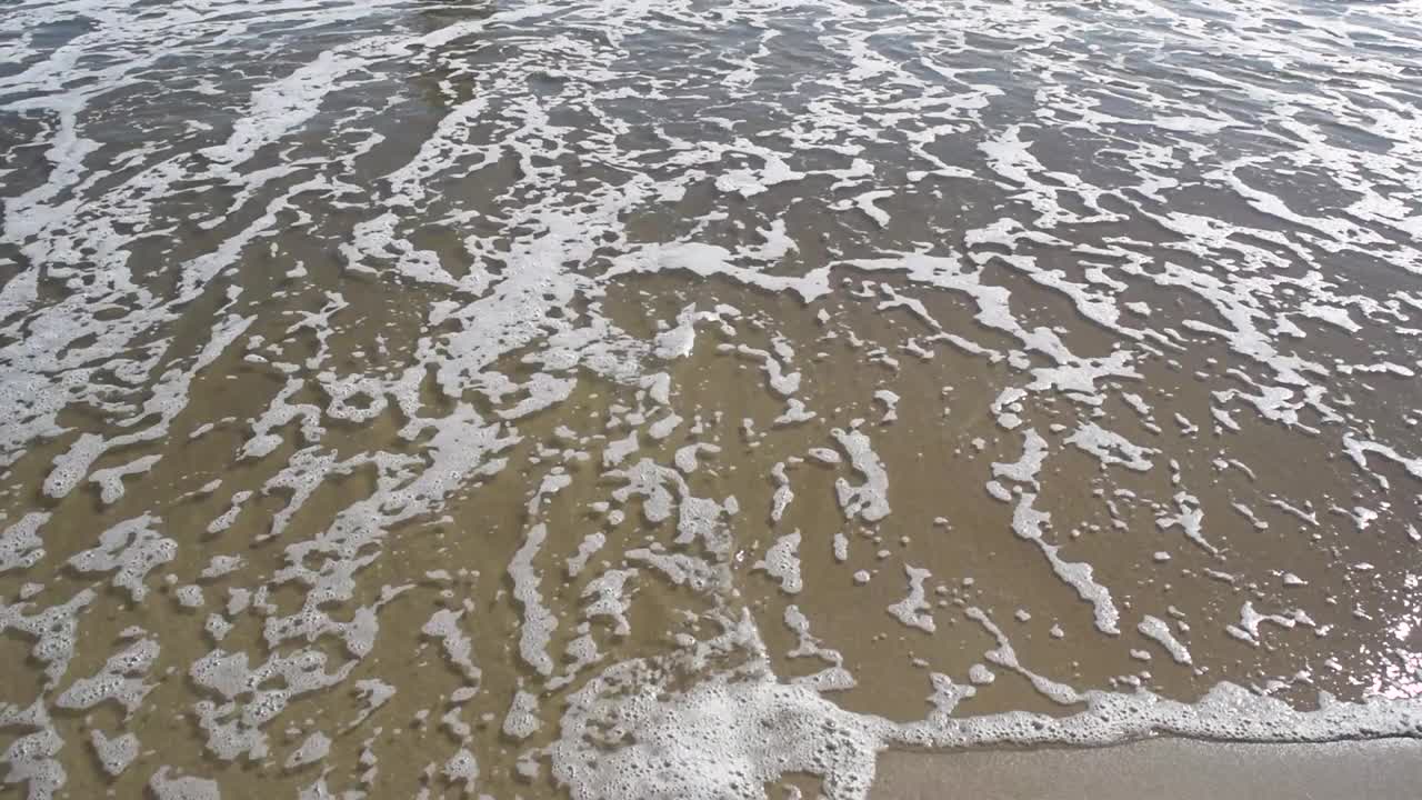 海浪的白色泡沫。海浪在沙滩上激起涟漪。海景特写。副本的空间。自然背景，文本模板。视频素材