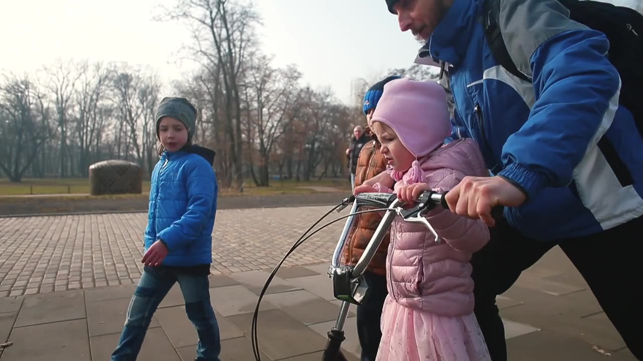 我女儿和她爸爸在城市公园里骑摩托车。他们在人行道上滚动。视频素材画面1