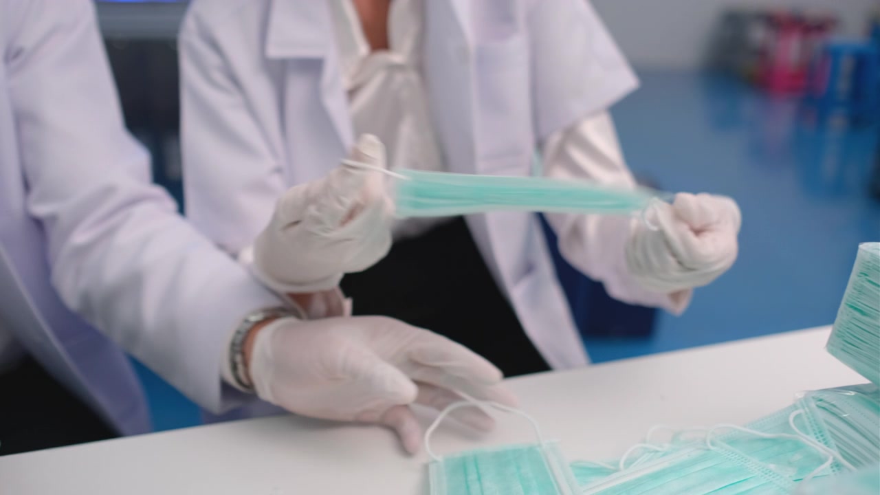关闭两名工厂或技术人员或工人的手与卫生口罩检查工作作为口罩产品的质量控制视频素材画面1
