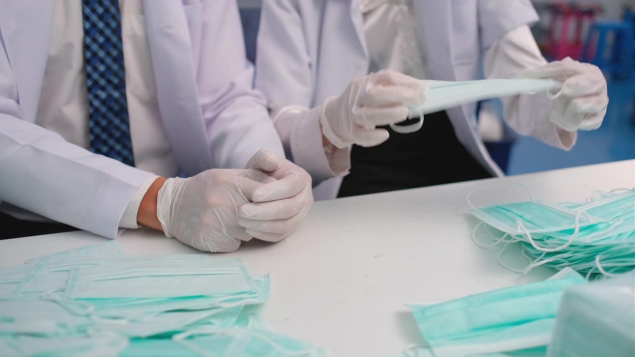 关闭两名工厂或技术人员或工人的手与卫生口罩检查工作作为口罩产品的质量控制视频素材画面2