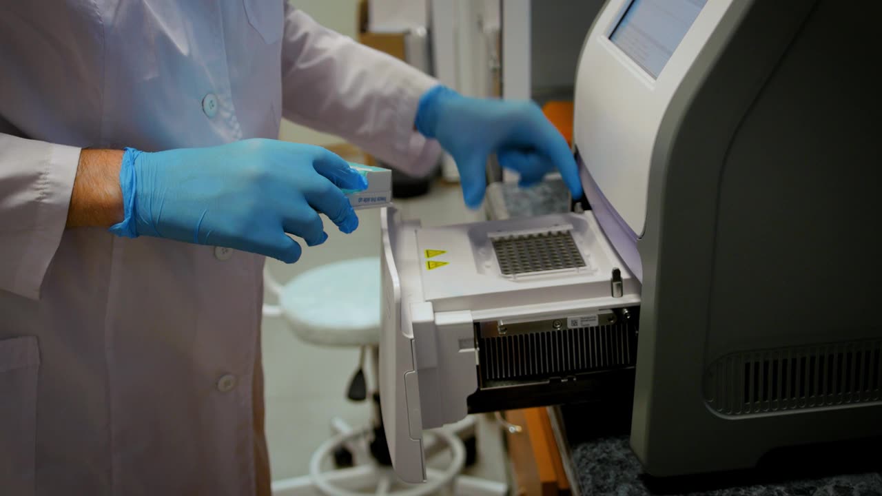 戴手套、穿白大褂的医生或科学家将装有试验品的试管装入仪器视频素材画面1