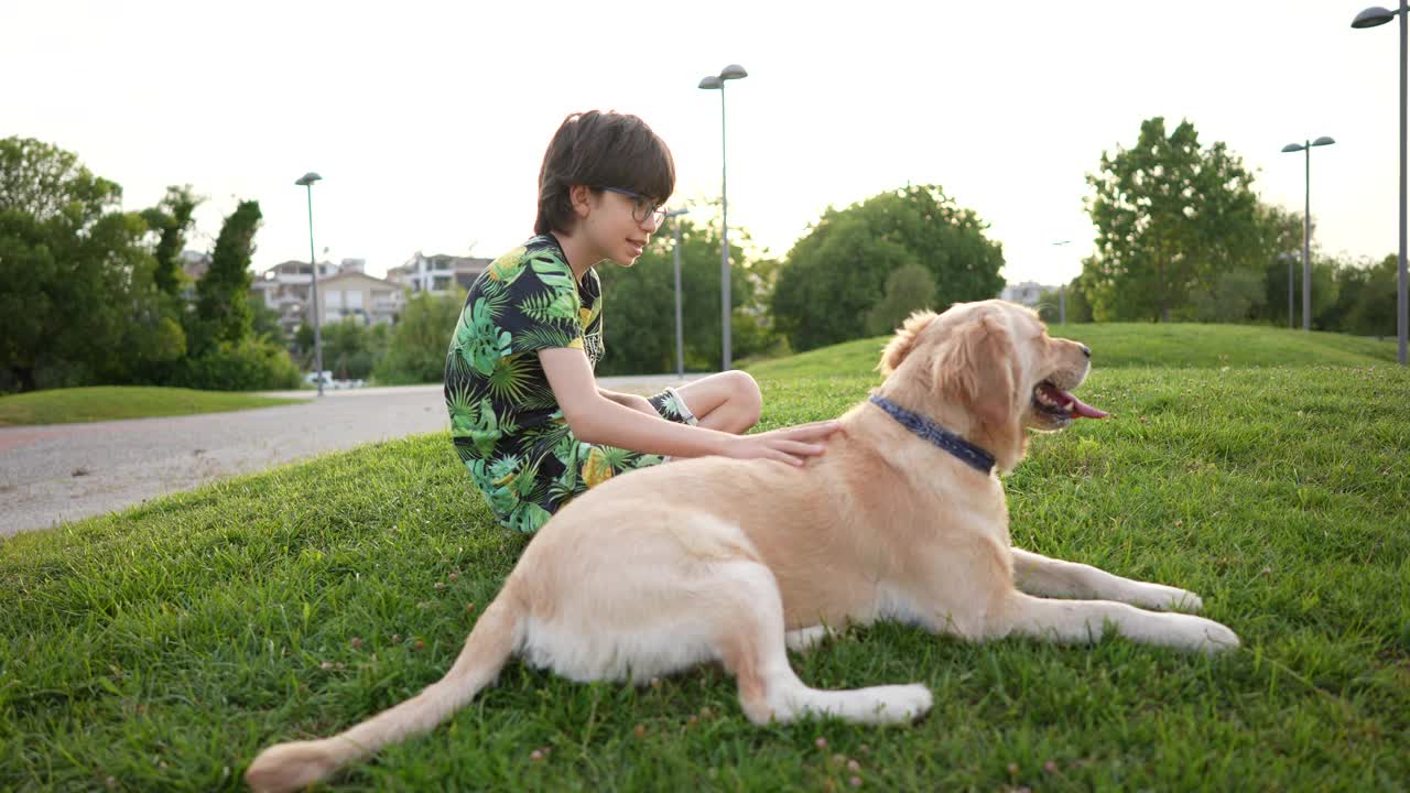 一个男孩和金毛猎犬坐在草地上。视频素材