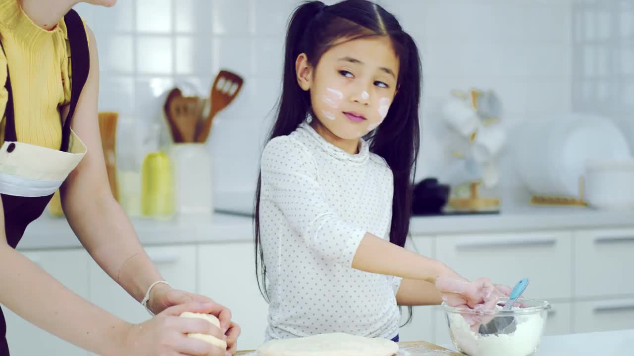 可爱的亚洲小女孩和美丽的妈妈，妈妈在家庭厨房的桌子上筛选面团面粉准备烘焙和蛋糕。泰国小孩像厨师一样玩面粉视频下载