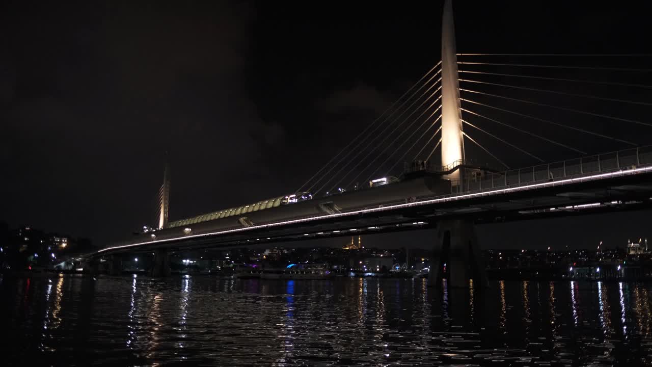 金角上的Halic桥高速公路大桥的夜景与黄色的灯光在Beyoglu，伊斯坦布尔在晚上的时间和一个小客轮漂浮在海上的城市景观城市视图黄昏海景概念4K分辨率视频素材