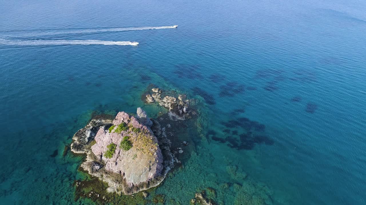 游艇在水中，一个孤独的岩石峰在公海，空中俯视图无人机4k拍摄。海洋撞击孤山岩石，旅游目的地，摩托艇上的活跃休闲，度假视频素材