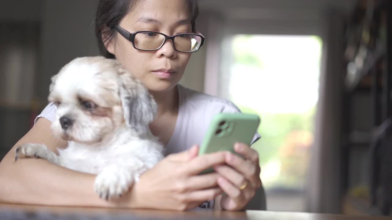 在家里的客厅里，一个女人和她的狗坐在一起输入智能手机视频素材