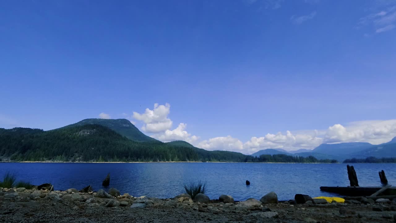 湖面上飘动的云朵和布满云杉树的山丘在流逝视频素材