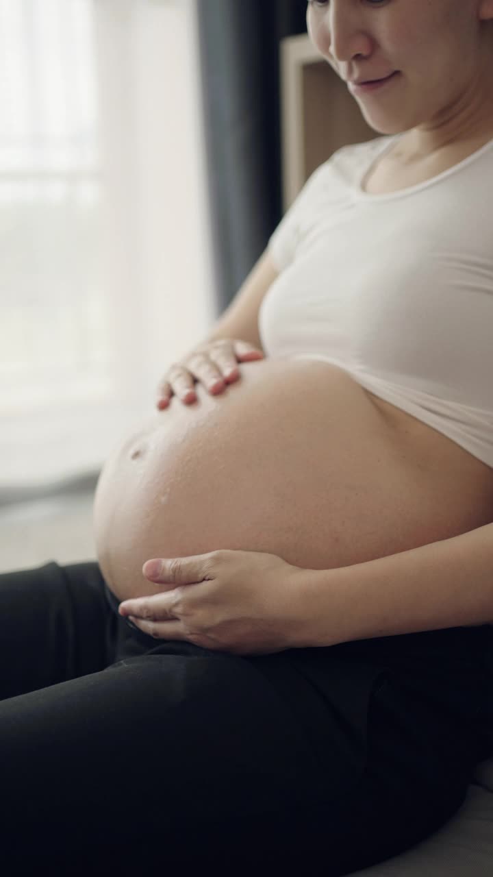 孕妇在家里把润肤霜涂在腹部视频素材