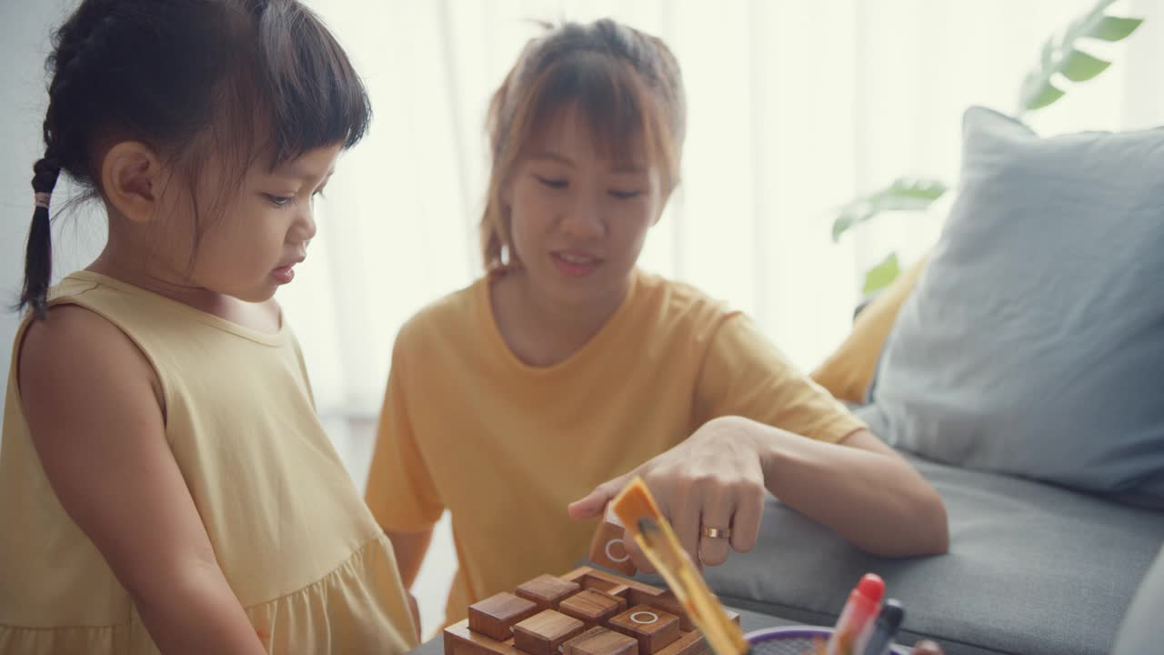 快乐开朗的亚洲家庭妈妈教女孩玩棋盘游戏的爱好，在家里的客厅沙发上放松。视频素材