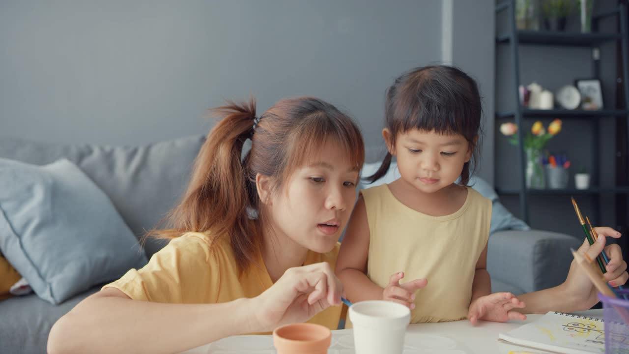 快乐快乐的亚洲家庭妈妈教学步的小女孩在家里客厅的桌子上画画，玩得开心放松。视频素材