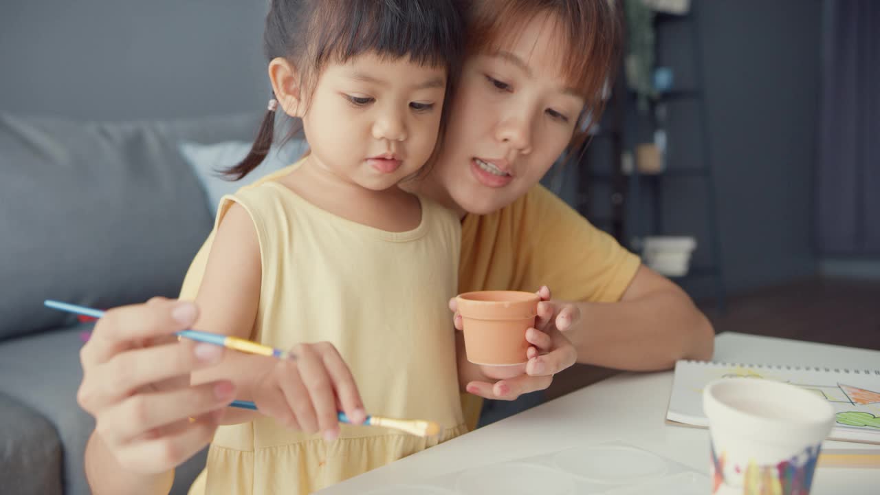 快乐快乐的亚洲家庭妈妈教学步的小女孩在家里客厅的桌子上画画，玩得开心放松。视频素材