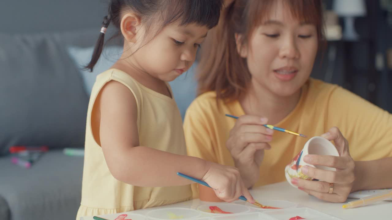 快乐快乐的亚洲家庭妈妈教学步的小女孩在家里客厅的桌子上画画，玩得开心放松。视频素材