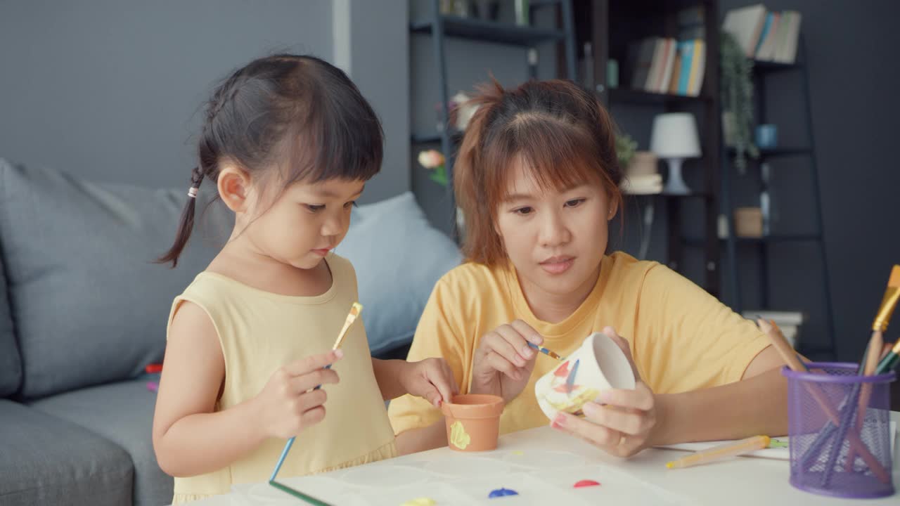 快乐快乐的亚洲家庭妈妈教学步的小女孩在家里客厅的桌子上画画，玩得开心放松。视频素材