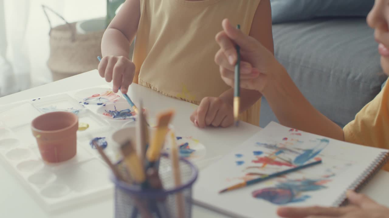 快乐快乐的亚洲家庭妈妈教学步的小女孩在家里客厅的桌子上画画，玩得开心放松。视频素材