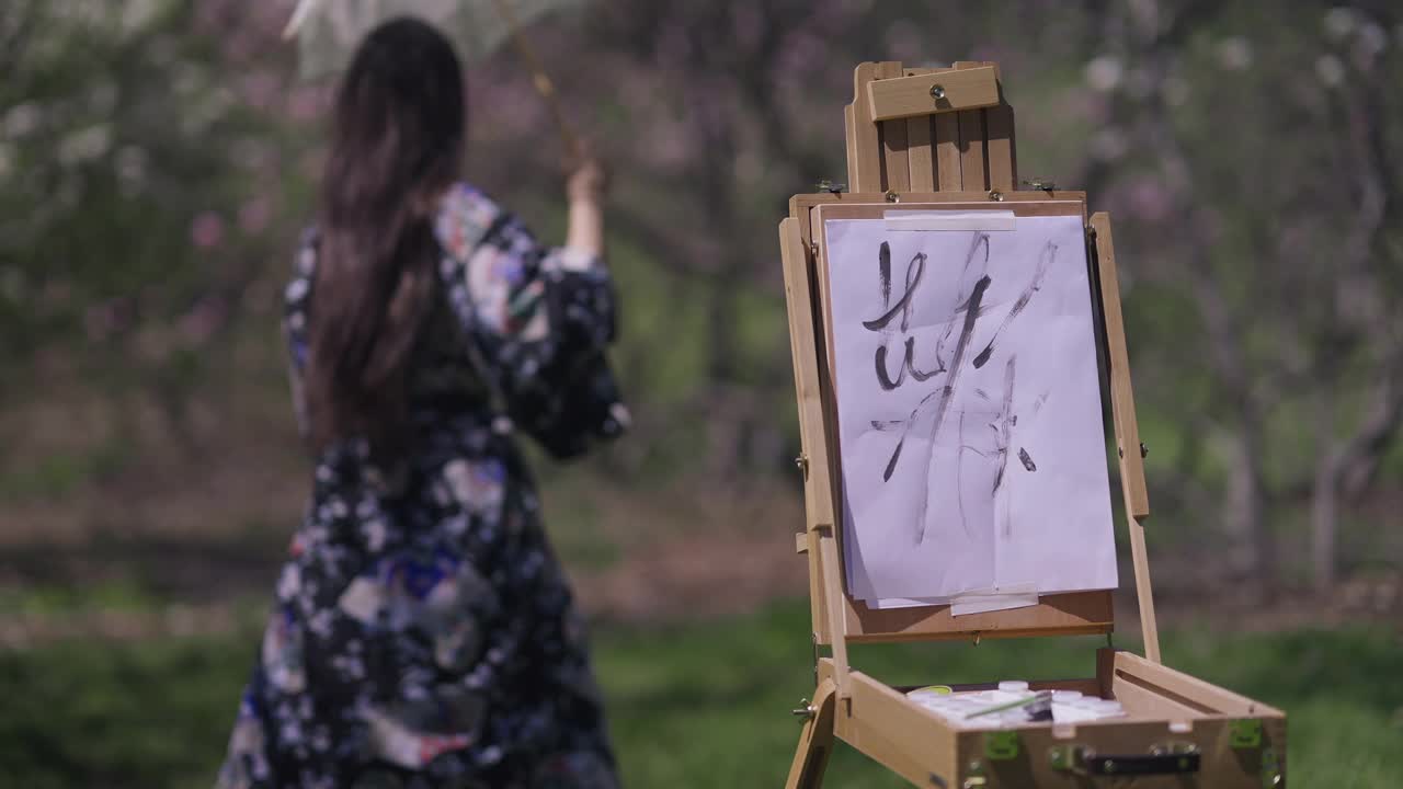 在阳光下画在画架上的画布，模糊的苗条的亚洲女人穿着和服，在白色太阳伞的背景下跳舞。快乐轻松的日本女士在阳光明媚的日子里享受春天的休闲。视频素材