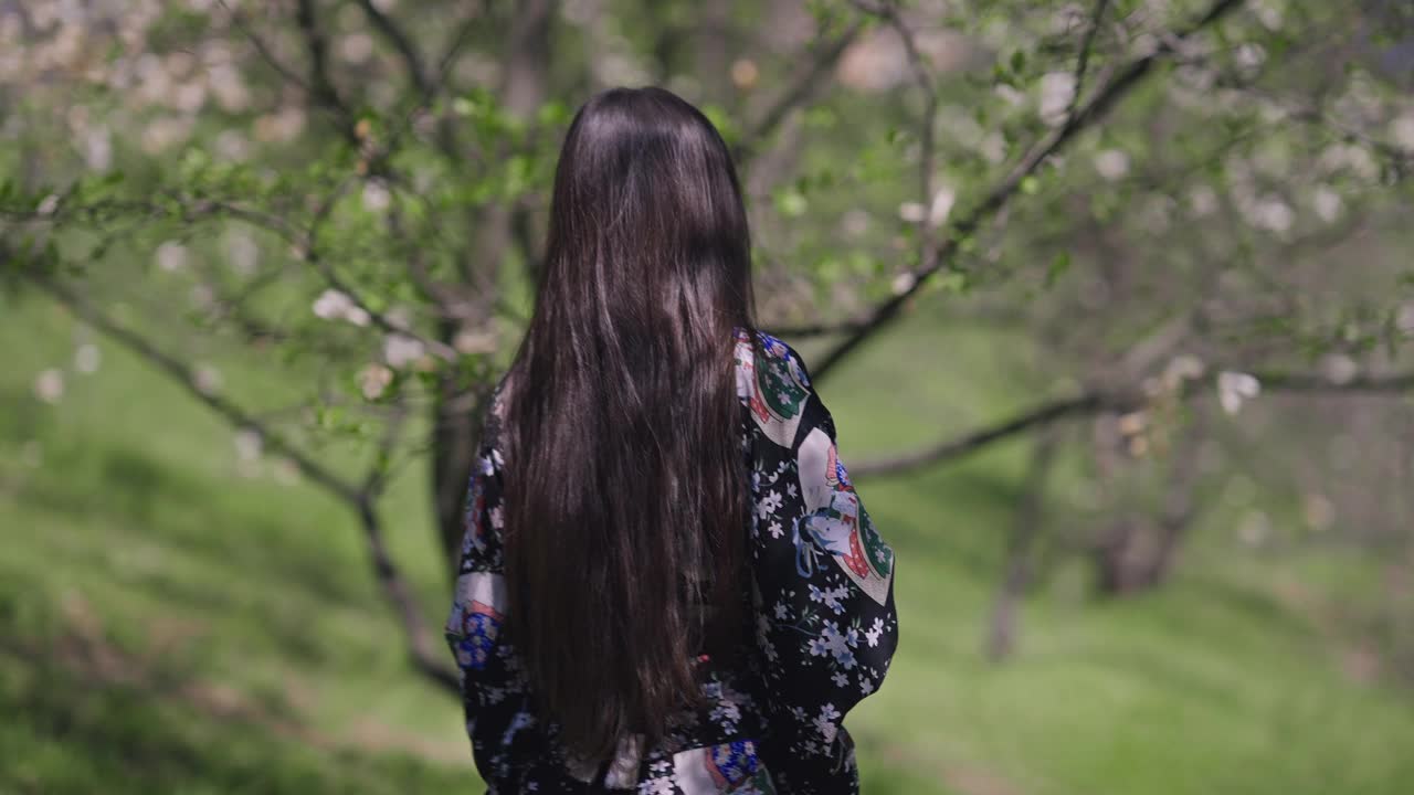 年轻苗条迷人的亚洲女子穿着和服走在阳光明媚的春天公园转身微笑看着相机。快乐自信的日本千禧一代享受户外自然之美。视频素材