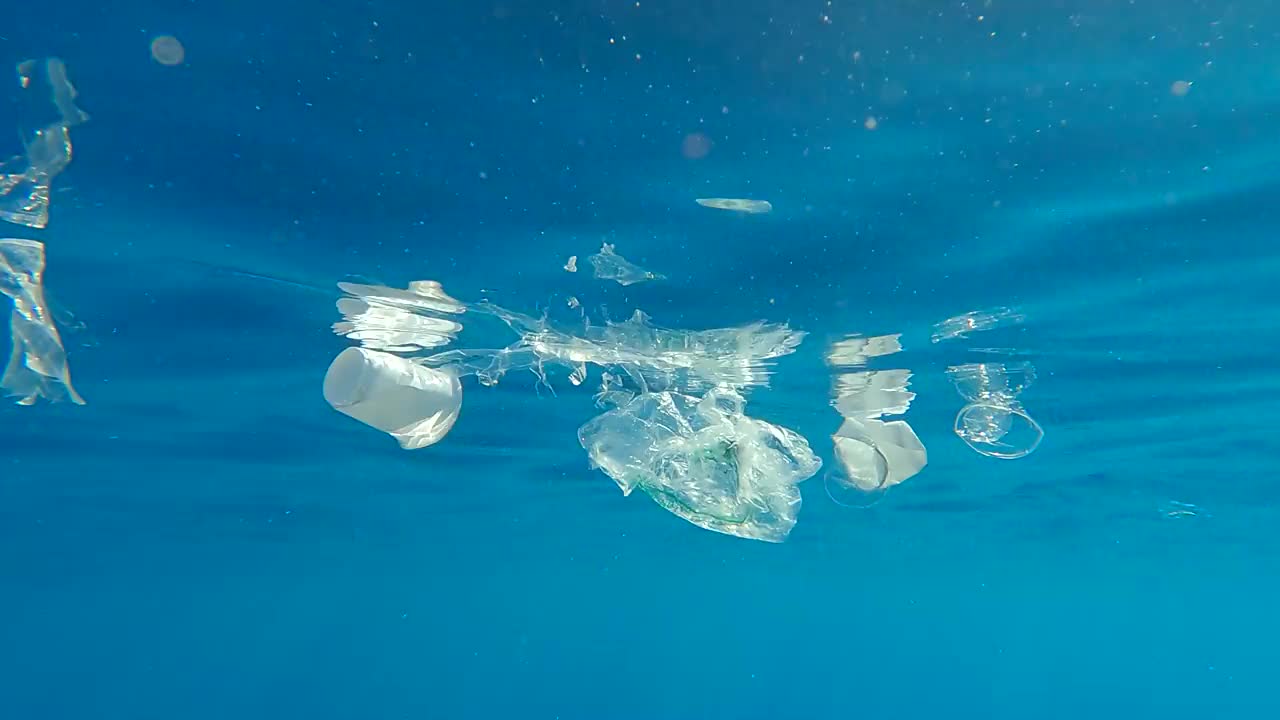 塑料盘子和塑料袋漂浮在蓝色的水面上，水下景色。海洋的塑料污染。(4 k-60pfs)。埃及红海视频素材