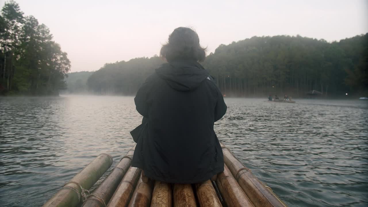 在泰国湄洪子邦雄，一名年轻的女游客坐在竹筏上，漂浮在湖面上，放松地享受大自然的美景视频素材