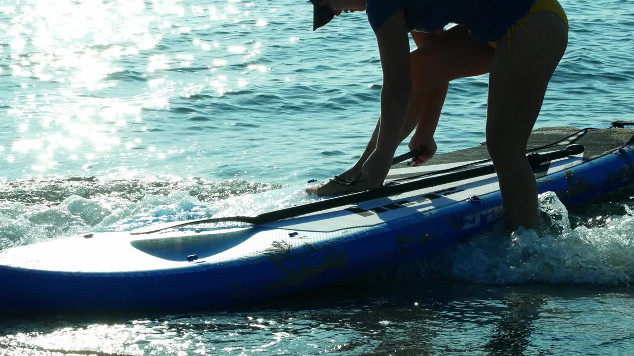 日出时分，一位身穿泳装的迷人年轻女子在冲浪板上冲浪。夏天，旅游，运动，冲浪板。视频素材