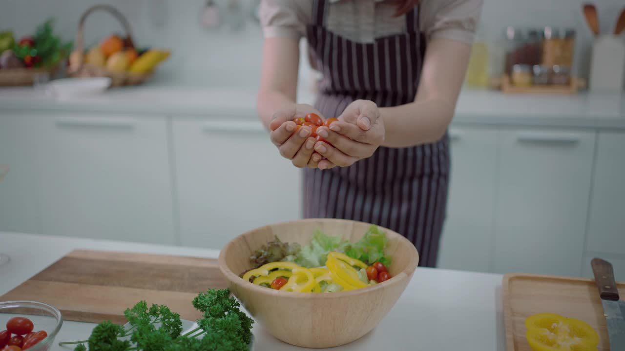 美丽的女人在家里为家人准备一顿饭，切不同的蔬菜做沙拉，看起来很开心-生活方式健康的饮食，健康的生活方式。视频素材