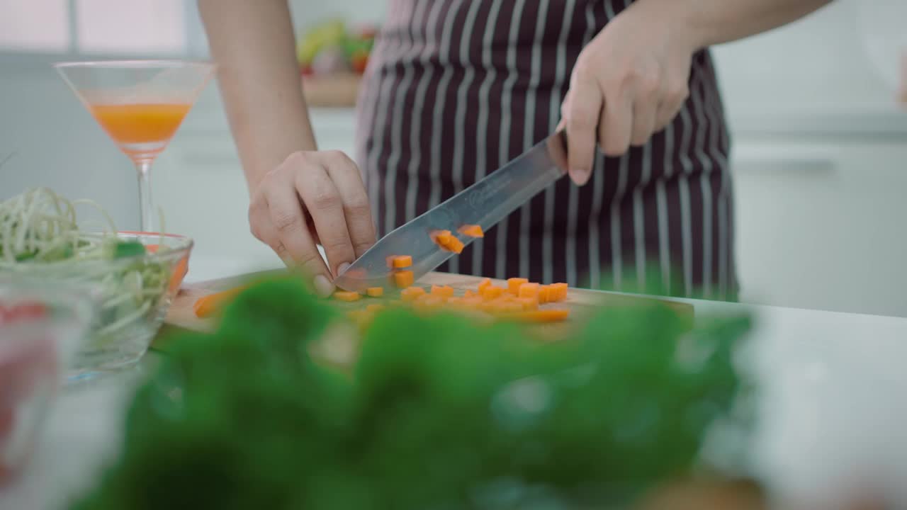 特写镜头:一名妇女在家里为家人准备一顿饭，她正在切不同的蔬菜做沙拉，看起来非常快乐——健康的饮食，健康的生活方式。视频素材