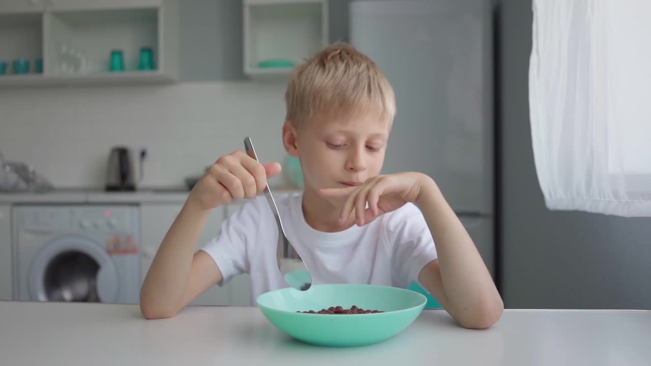 可爱的男孩在上学前吃早餐，有麦片和牛奶。小学生在厨房视频素材