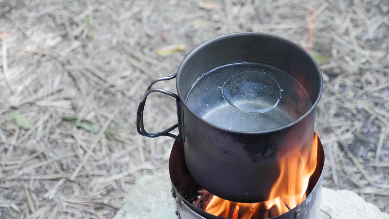 烹饪对自然。在柴火炉子上加水的锅中加入一小撮盐。露营生活。旅游和旅游理念。烹饪着火了视频素材