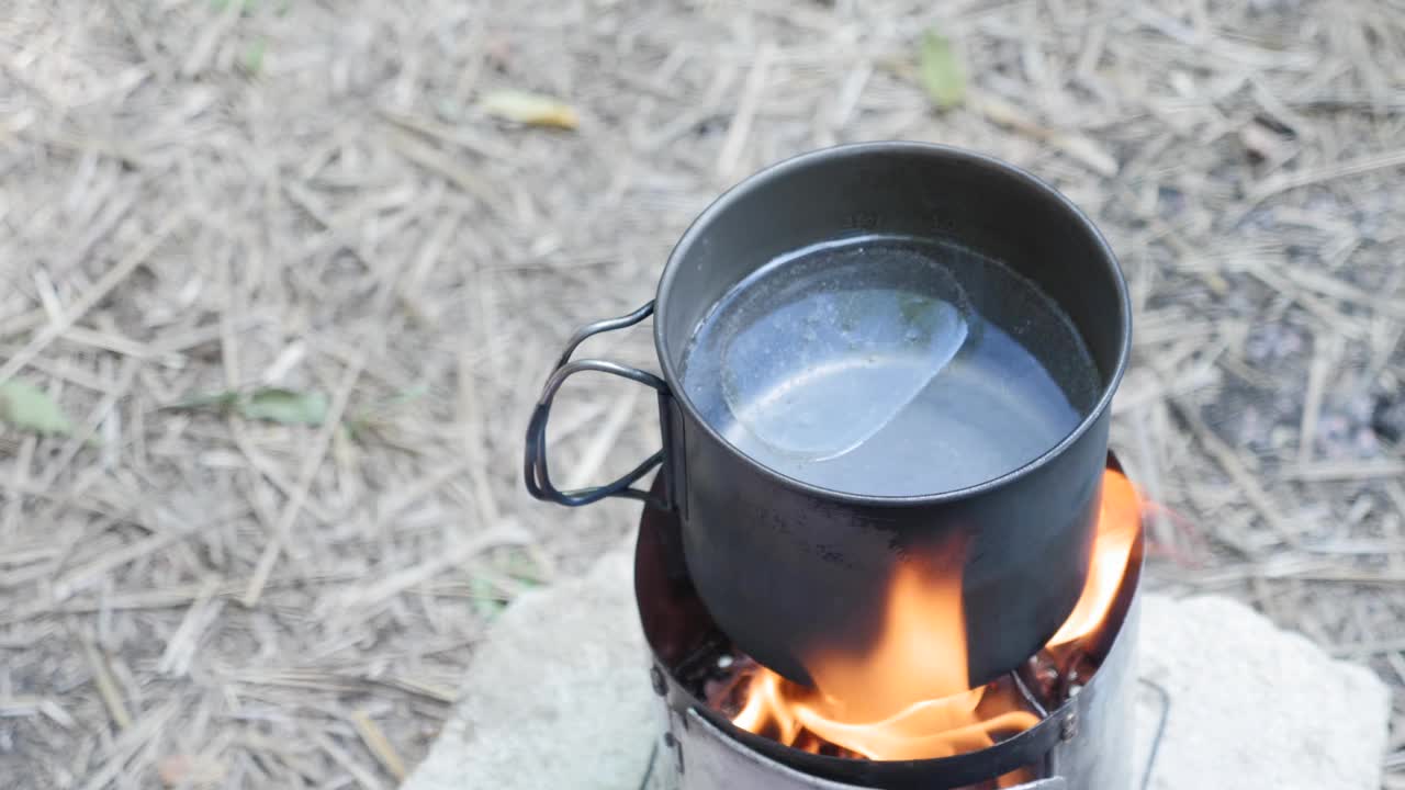 烹饪着火了。女人在大自然中准备食物。用手把胡萝卜和洋葱放入烧着的炉子上的水锅中。露营生活。旅游的概念视频素材