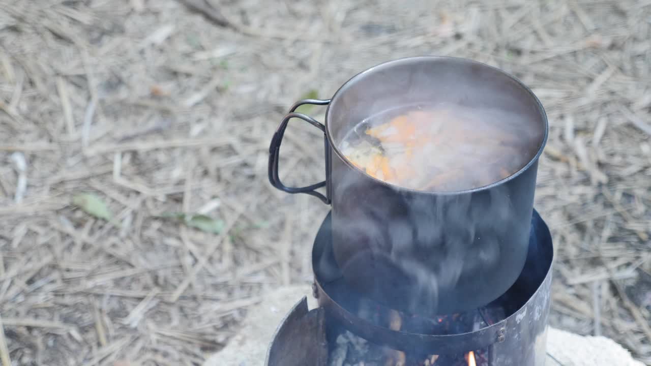 烹饪着火了。游客在燃烧木柴的炉子上准备露营食物。用手把谷物放进烧开的水壶里视频素材