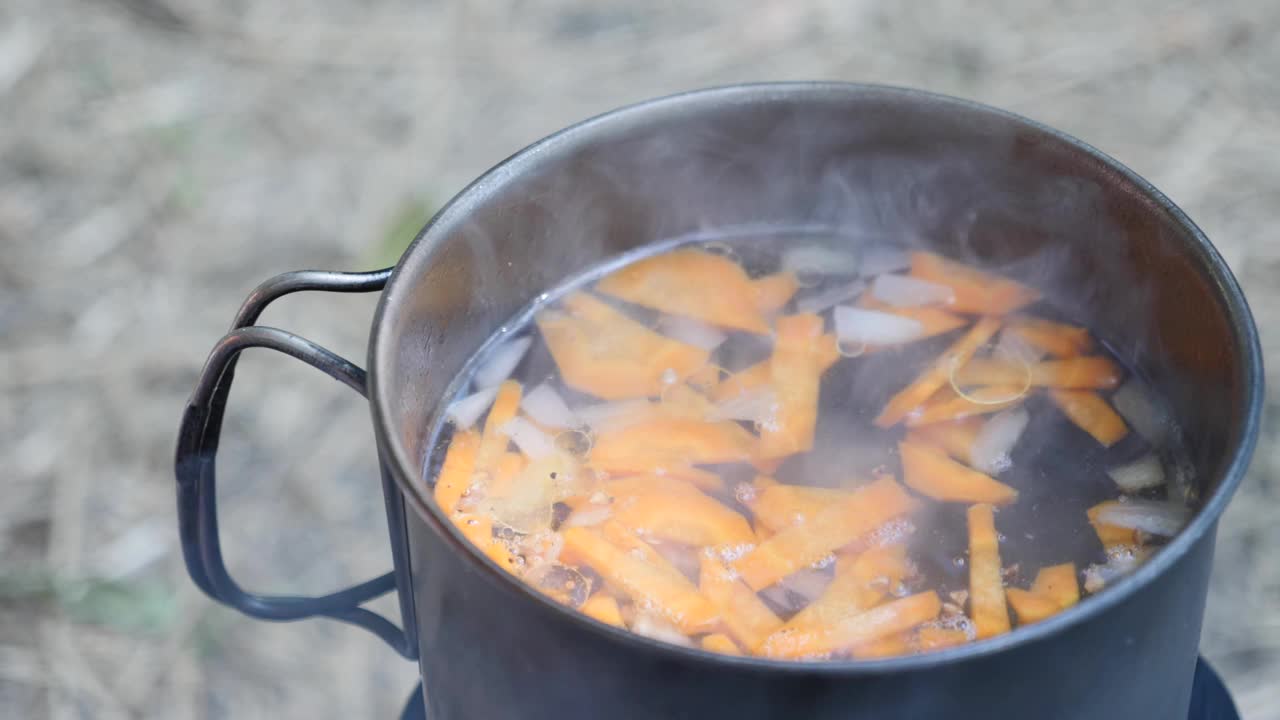 在火上把谷物加入沸水中。烹饪对自然。在燃烧的炉子上准备野营食物。旅游营的游客烹饪视频素材