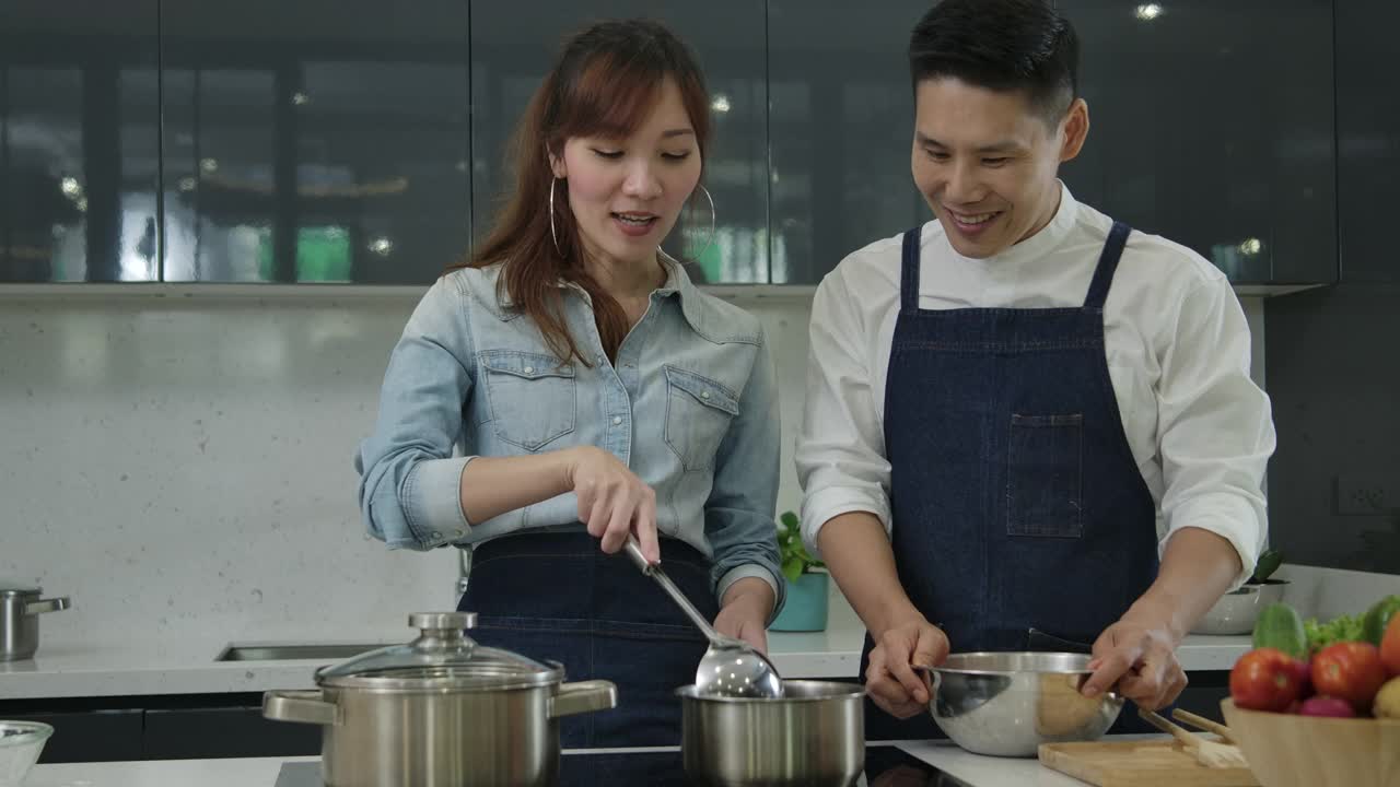 年轻的亚洲妻子和丈夫一起在厨房跳舞和努力做饭。视频素材