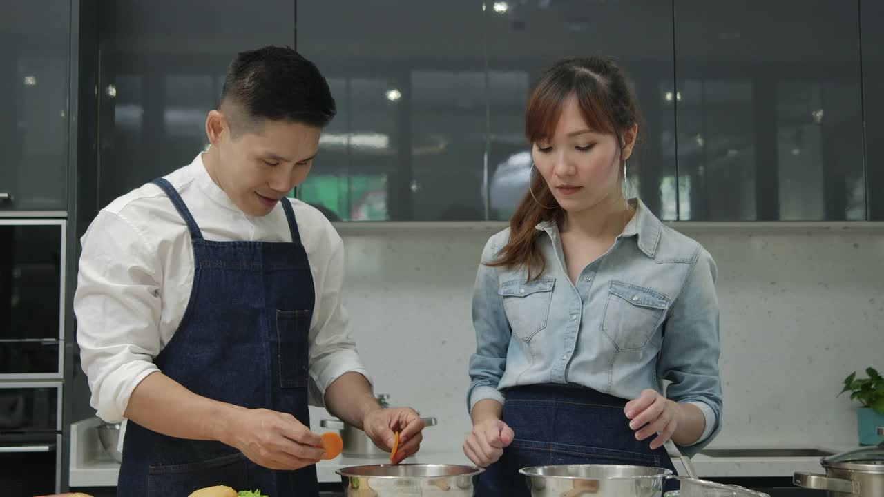 年轻的亚洲妻子和丈夫一起在厨房跳舞和努力做饭。视频素材