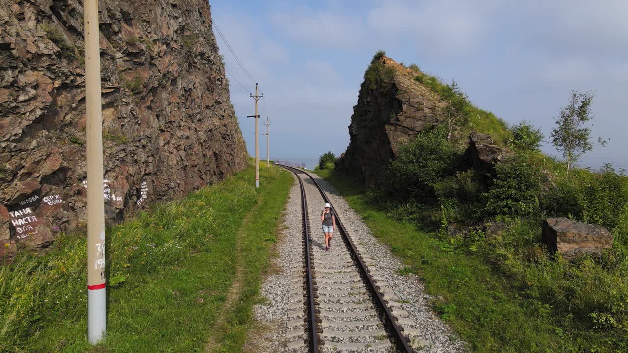 4K女旅行者，背着背包，夏日漫步在铁路的铁轨上。视频素材