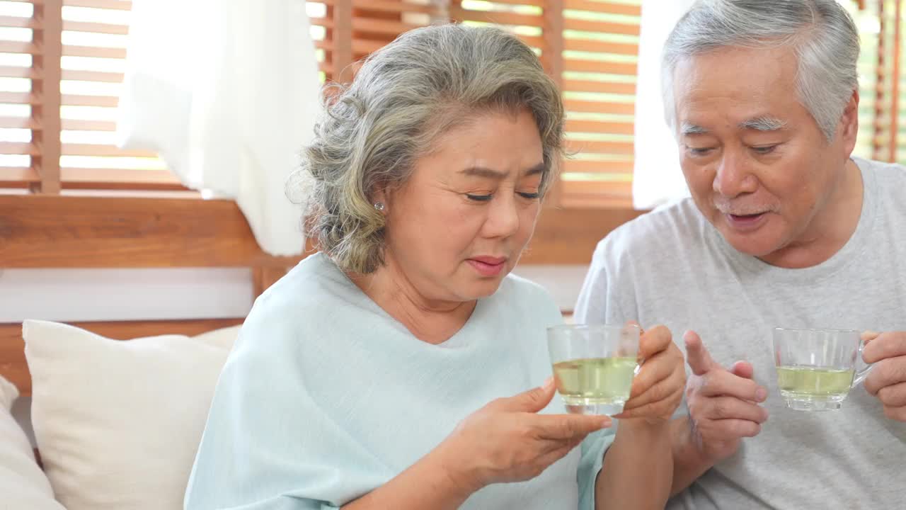 4K亚洲老夫妇坐在沙发上，一起在客厅喝花草茶。视频素材